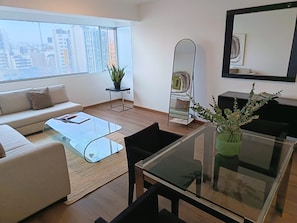 A modern living room with a sofa, coffee table, and a large window offering a city view.