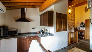 A kitchen with wooden cabinets, a microwave, a sink, and a stone wall.