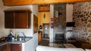 A kitchen with wooden cabinets, a stone wall, a fireplace, and a television mounted on the wall.