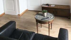 A living room with a flat-screen TV mounted on the wall, a round coffee table with a plant, and a wooden cabinet. - Attractive 32 M2 studio with 12 M2 private courtyard (Dinard)