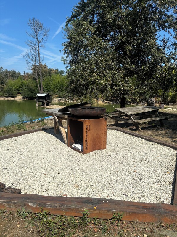 Un área de picnic con una parrilla, un banco de madera y un pequeño refugio junto a un lago.