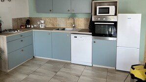 Una cocina compacta con armarios azul claro, un lavavajillas blanco, un microondas y un refrigerador.