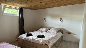 Un dormitorio con cama de madera, una mesita de noche pequeña, una lámpara de noche y una ventana con cortinas, además de techo de madera.