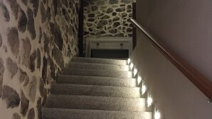 A staircase with stone walls and a wooden handrail, leading to a room with a stone ceiling and a bed. - Apartamento Manhegu (Trevejo)