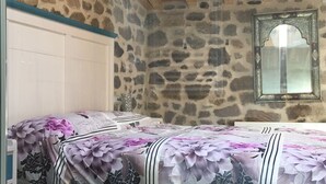 A bedroom with a stone wall, a bed with floral bedding, a white wardrobe, and a mirror with an ornate frame. - Apartamento Manhegu (Trevejo)