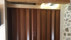 A wooden wardrobe with vertical slats and two handles, located in a room with a stone-patterned wall and a visible radiator. - Apartamento Manhegu (Trevejo)