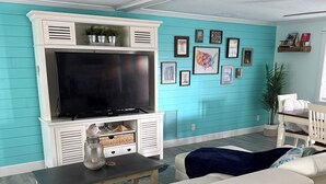 A living room with a large flat-screen TV, a white sofa, a coffee table, and a teal accent wall.