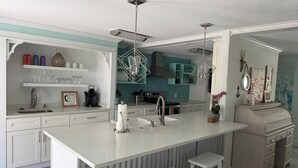 A modern kitchen with a central island, white cabinetry, and a teal backsplash.