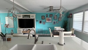 A modern kitchen with a double sink, a large TV, and a dining area with a table and chairs.
