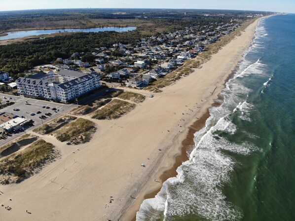 An aerial view of a coastal residential area with a beachfront, a large hotel, and a road leading to the beach.