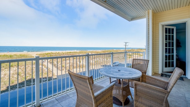 A covered patio with a table and chairs, overlooking a beach. - Book Beach Haven 213D | Oceanfront Sandbridge Rental (Virginia Beach)