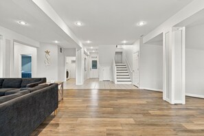 Un vaste espace de vie doté d’un canapé gris foncé, de parquet et d’un escalier menant à un deuxième étage.