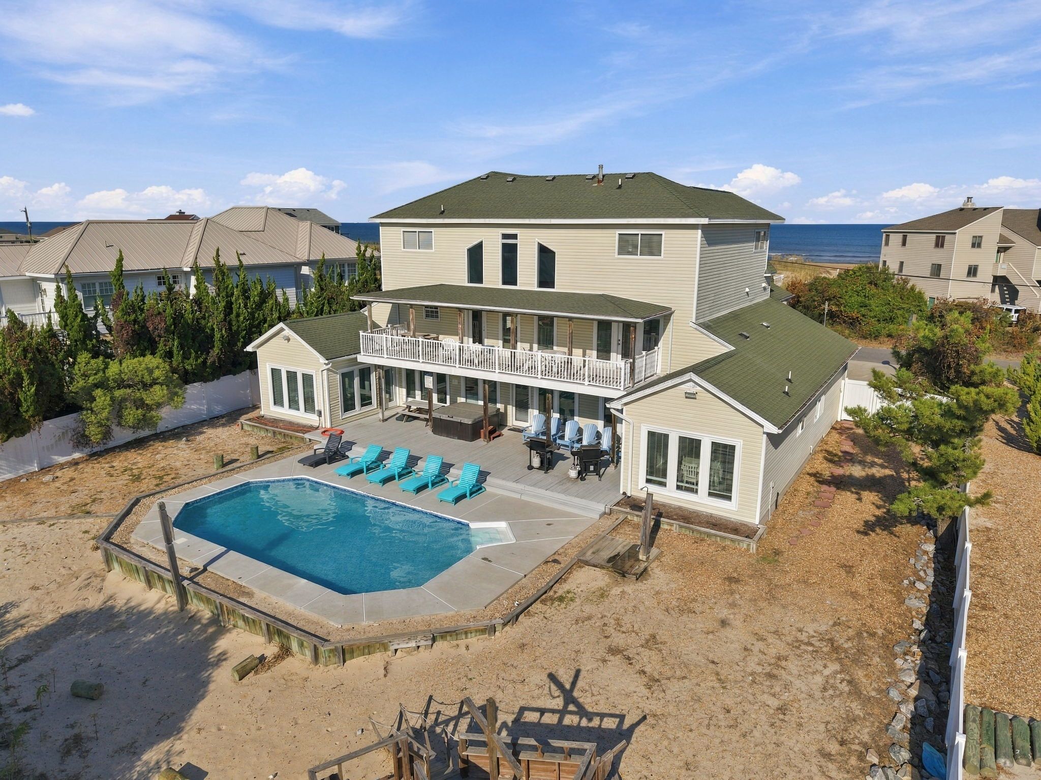 A two-story house with a large backyard featuring a swimming pool, outdoor seating, and a view of the ocean.