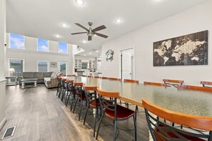A spacious dining area with a long table and chairs, a ceiling fan, and a world map on the wall. - Book Spinnaker | Semi-Oceanfront Sandbridge Vacation Rental (Virginia Beach)