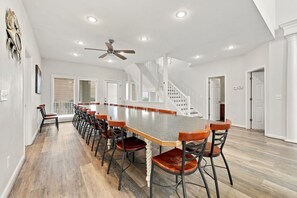 A spacious room with a long dining table, multiple chairs, a ceiling fan, and a staircase. - Book Spinnaker | Semi-Oceanfront Sandbridge Vacation Rental (Virginia Beach)