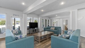 A spacious living room with teal sofas, a wooden coffee table, and a television. - Book Spinnaker | Semi-Oceanfront Sandbridge Vacation Rental (Virginia Beach)