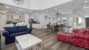 A spacious living area with a kitchen, dining area, and a staircase leading to an upper level. - Book Spinnaker | Semi-Oceanfront Sandbridge Vacation Rental (Virginia Beach)