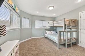 A child's bedroom with bunk beds, a white dresser, and a window with blinds. - Book Spinnaker | Semi-Oceanfront Sandbridge Vacation Rental (Virginia Beach)