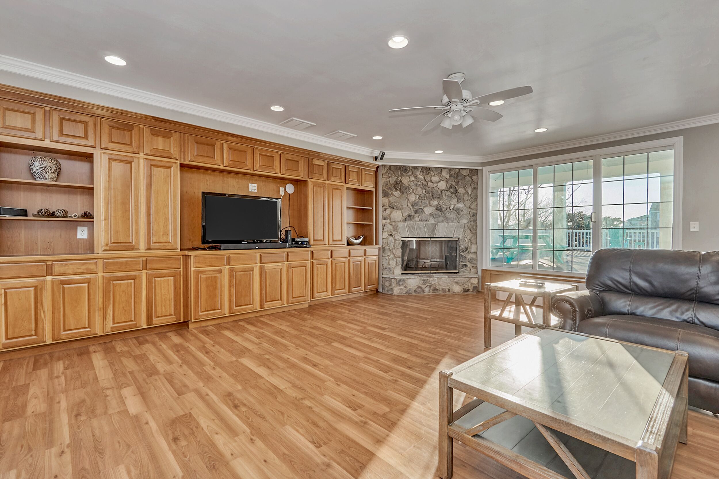 A spacious living room with wooden cabinets, a flat-screen TV, a stone fireplace, and a leather couch.