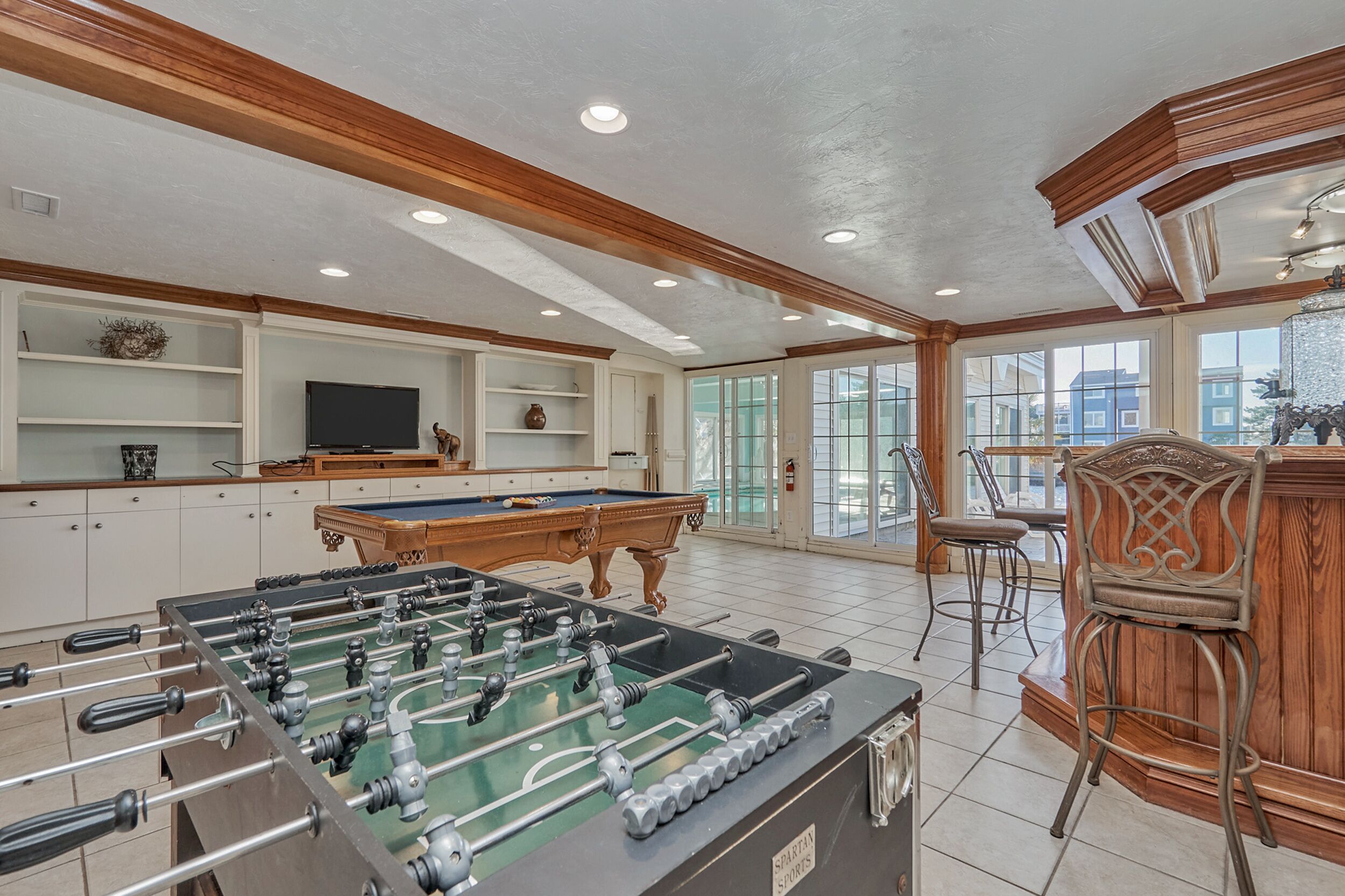 A room with a pool table, a foosball table, and a bar area with chairs.