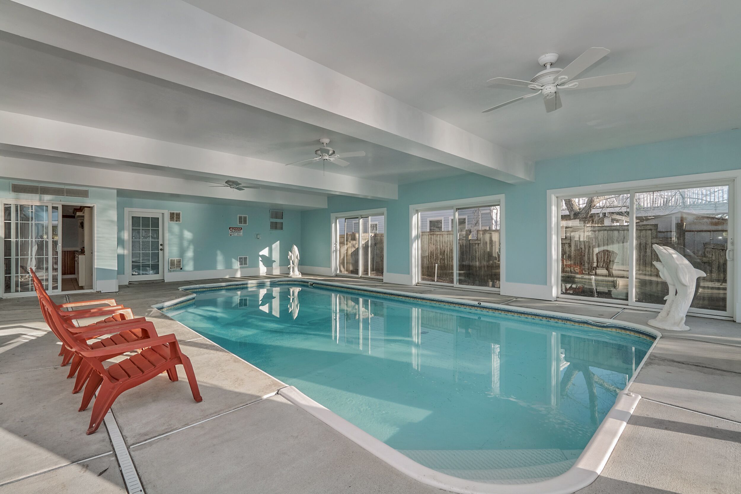 A swimming pool with a ceiling fan, a statue, and a view of the backyard.