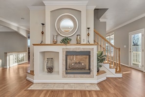 A spacious living area with a fireplace, a staircase, and a large mirror on the wall. - Luxurious Beach Home with Indoor Pool Access! Steps from the Beach (Virginia Beach)
