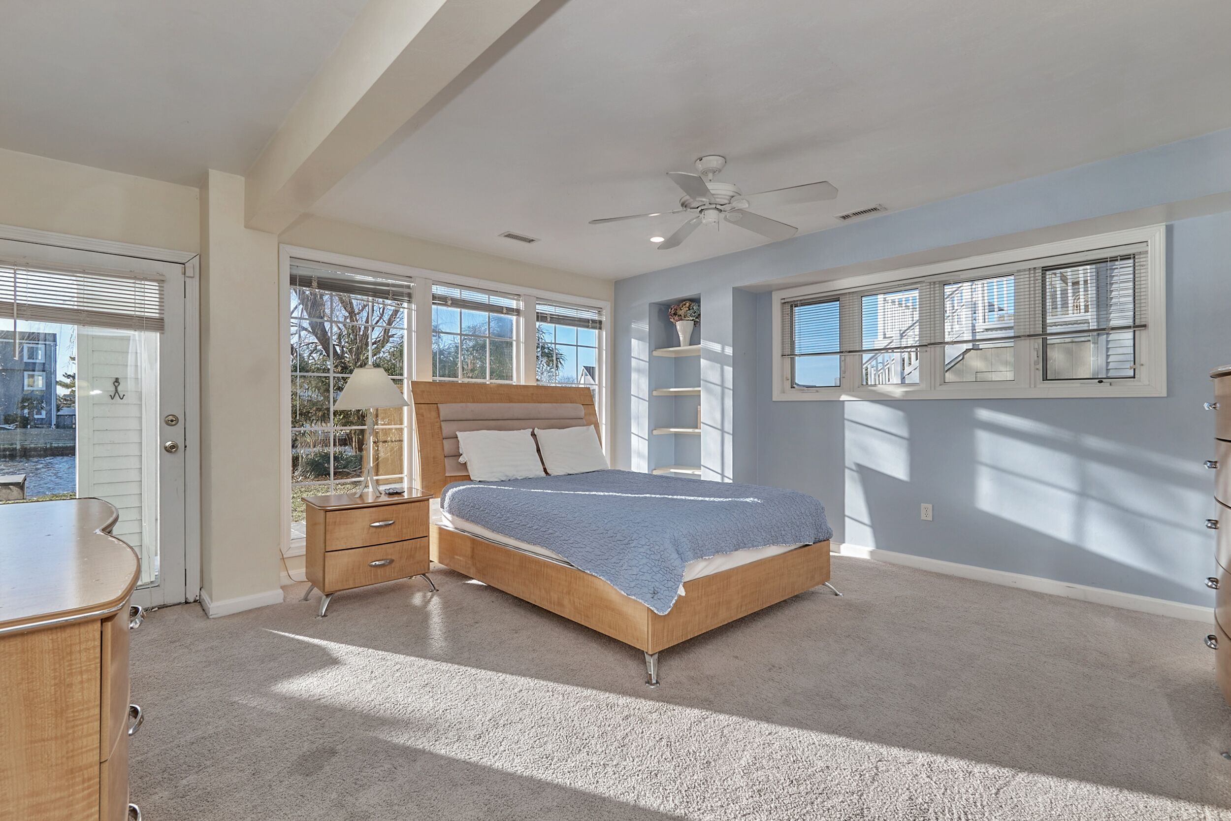 A bedroom with a bed, a dresser, a nightstand, a ceiling fan, and a window with blinds.