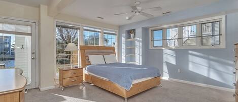 A bedroom with a bed, a dresser, a nightstand, a ceiling fan, and a window with blinds.