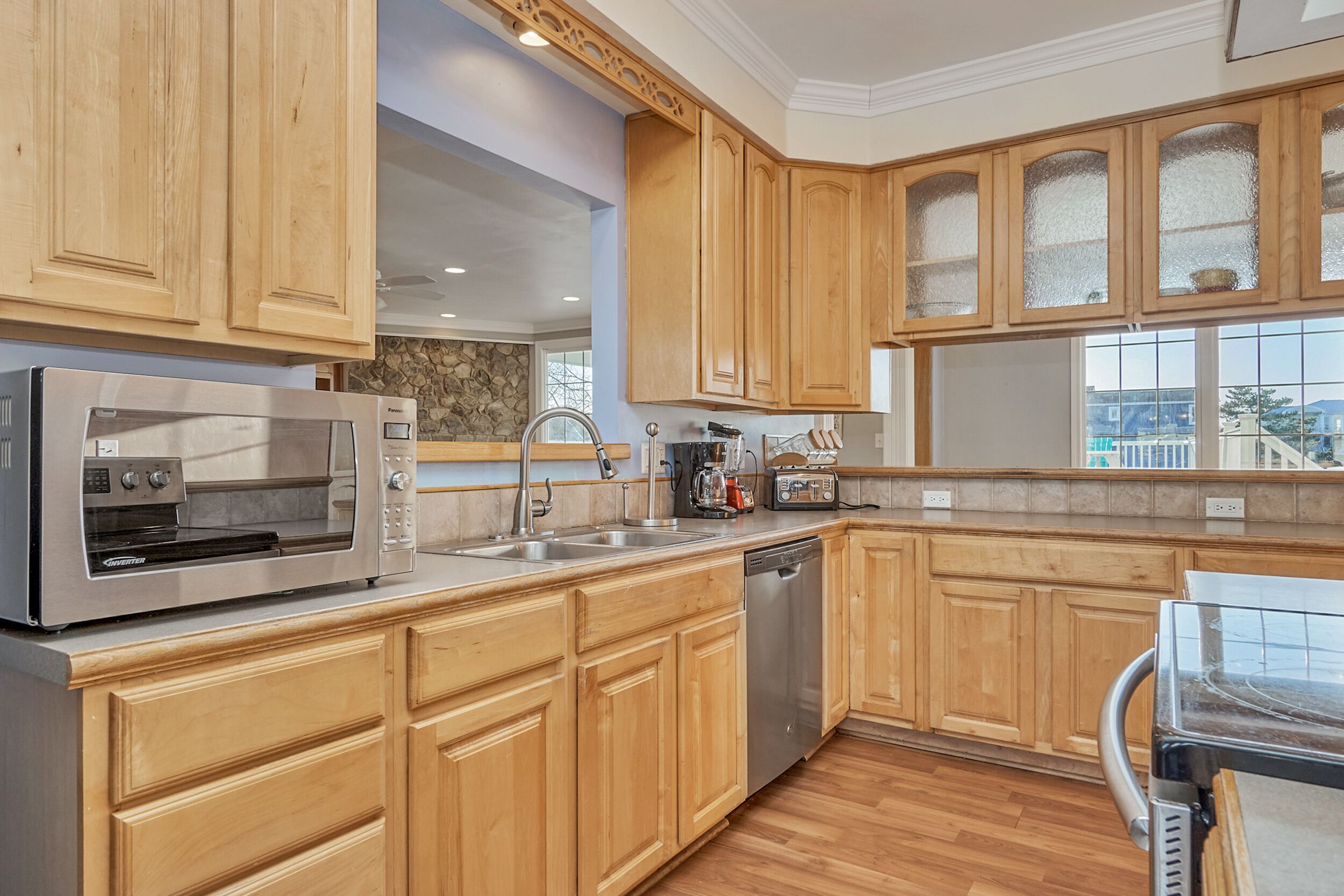 A modern kitchen with wooden cabinets, a stainless steel microwave, a dishwasher, and a window overlooking a cityscape.