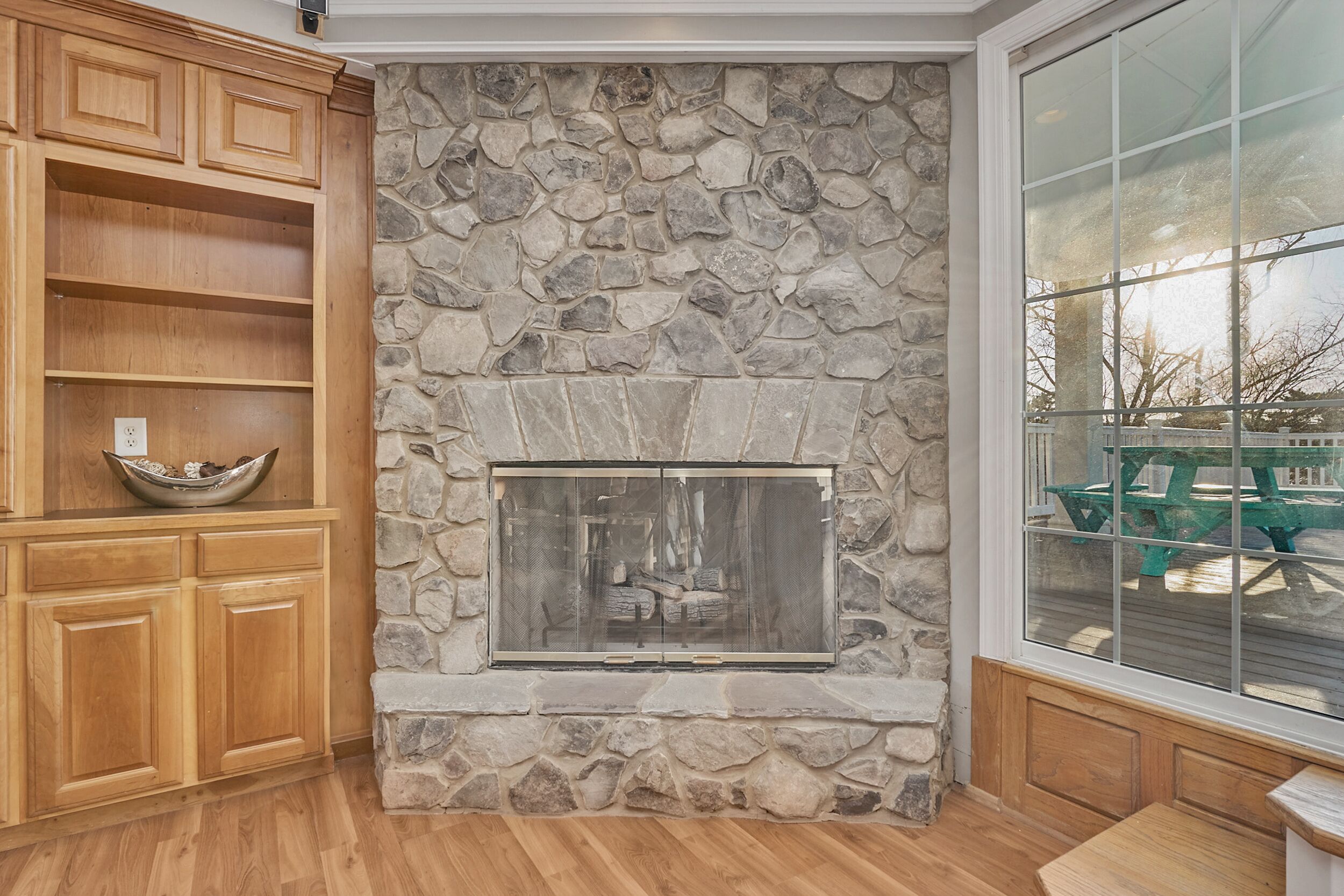A stone fireplace with a glass door, wooden cabinets, and a large window.
