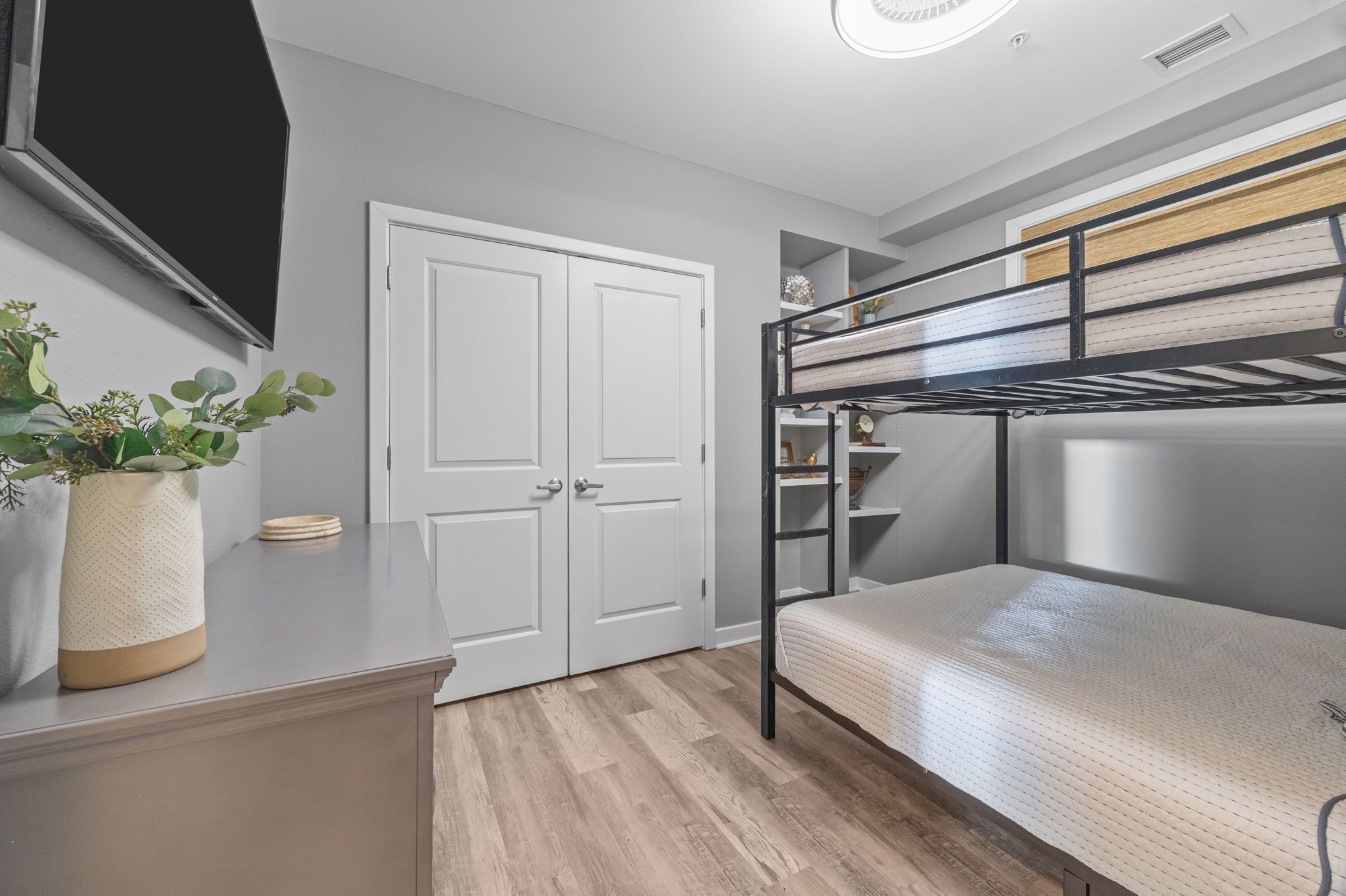 Ein Schlafsaalzimmer mit Etagenbetten, einer weißen Tür, einer kleinen Pflanze und einem Schreibtisch.