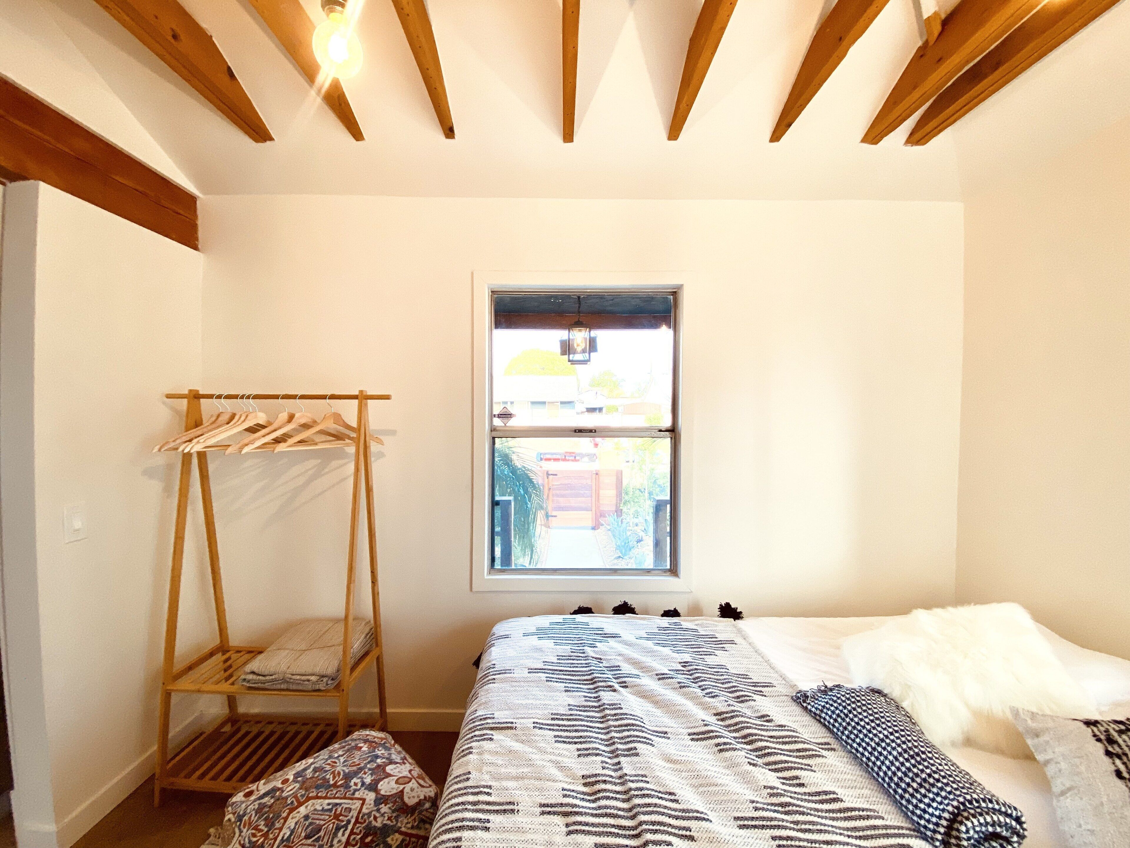 A bedroom with a wooden bed, a window, and a wooden drying rack.