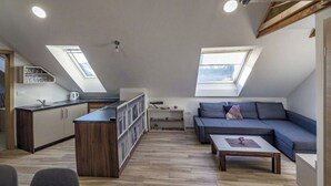 Een ruimtelijk ingerichte leefruimte met kitchenette, een bank, een eethoek en dakramen.