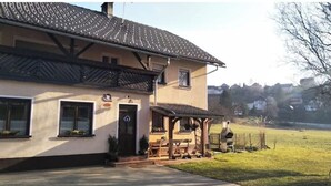Een gebouw met twee verdiepingen, een pannendak, een overdekte veranda en een kleine tuin.