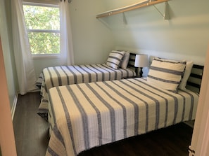 A room with two beds, each with striped bedding, a bedside table with a lamp, and a window with curtains.