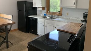 Una cucina compatta con mobili bianchi, un frigorifero nero, una lavastoviglie, un lavello e un piano cottura.
