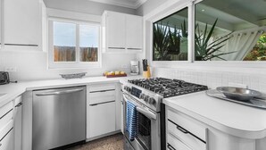 Une cuisine moderne avec des meubles blancs, un lave-vaisselle en acier inoxydable, une cuisinière à gaz et une grande fenêtre donnant sur l’extérieur.