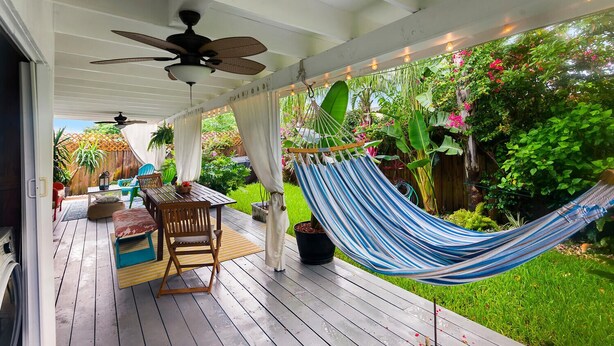 Un patio couvert avec un hamac, des meubles en bois et un ventilateur de plafond.