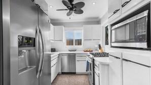 Une cuisine moderne dotée d’appareils électroménagers en acier inoxydable, de meubles blancs, d’une cuisinière à gaz et d’un ventilateur de plafond.