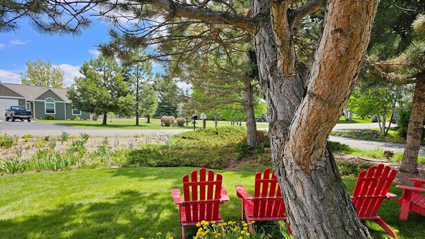 Un jardin avec des fauteuils Adirondack rouges, une pelouse et une maison en arrière-plan.