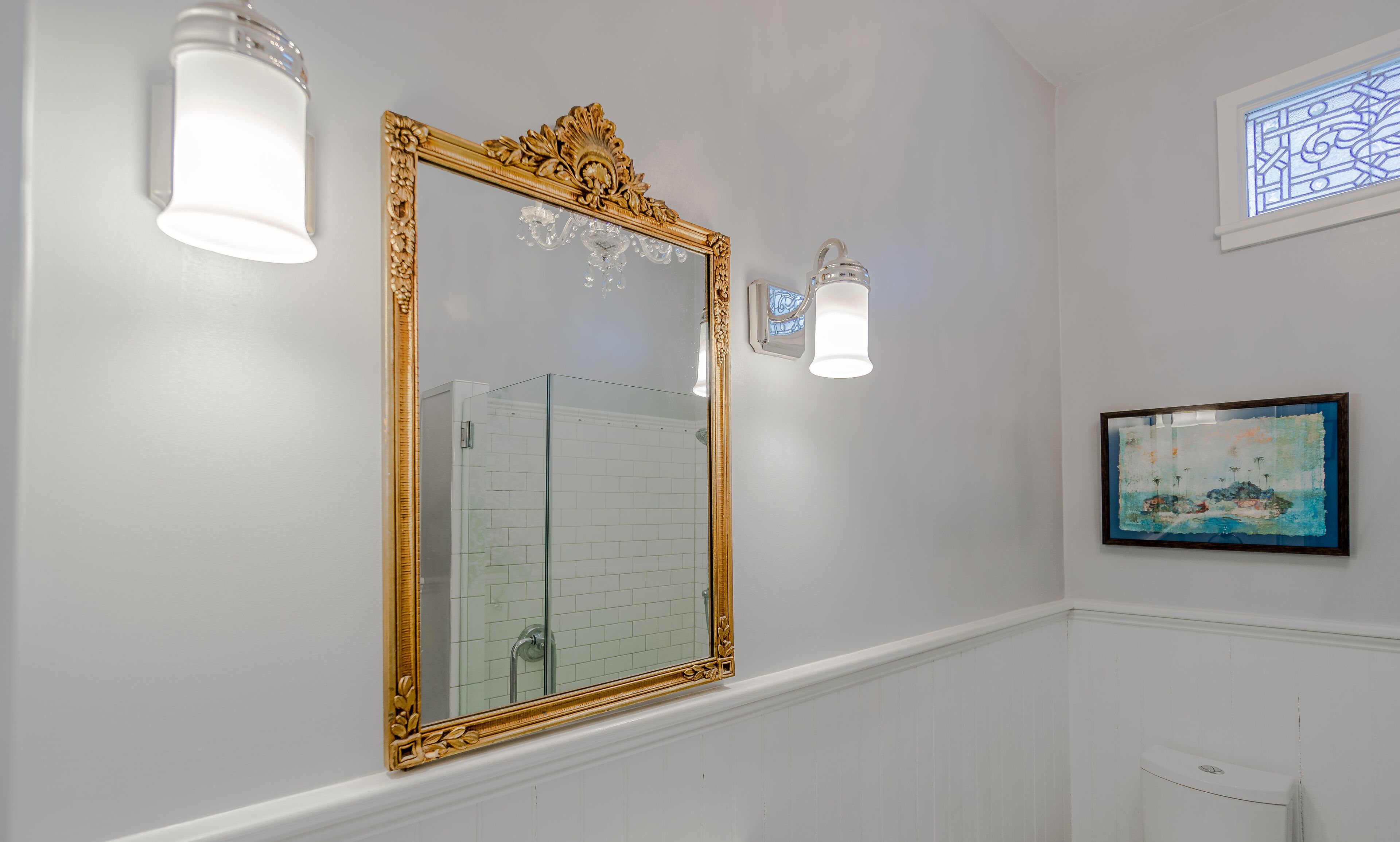 Een badkamer met een grote, versierde spiegel, witte wanden en een betegelde douchehoek.