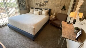 A neatly arranged hotel room with a large bed, a small desk, a chair, and a mirror. - Cabernet Cottage (Cottonwood)