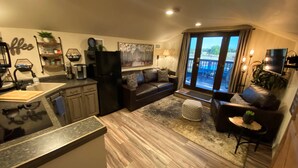 A modern kitchen with a refrigerator, coffee maker, and a sink. There is a dining area with a table and chairs, and a living room with a sofa and a television. - Cabernet Cottage (Cottonwood)