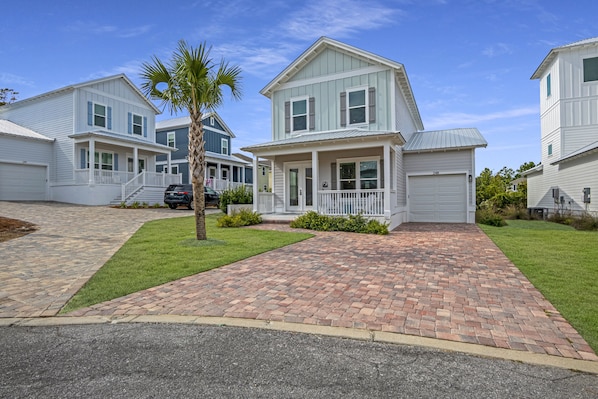 A residential neighborhood with white houses, a paved driveway, and a palm tree.