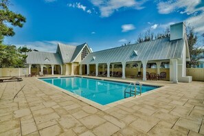 A pool area with a clear blue pool, lounge chairs, and a covered seating area with a metal roof.