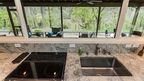 Una cucina con piano cottura integrato, lavello e finestra vista su una zona boschiva.