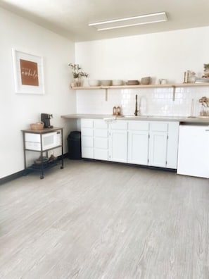 A modern kitchen with white cabinets, a wooden countertop, and a hanging shelf with bowls and plants.