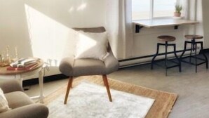 Een moderne woonkamer met een bank, een kleintje tafeltje met boeken, een aan de muur bevestigde televisie en een raam met gordijnen.