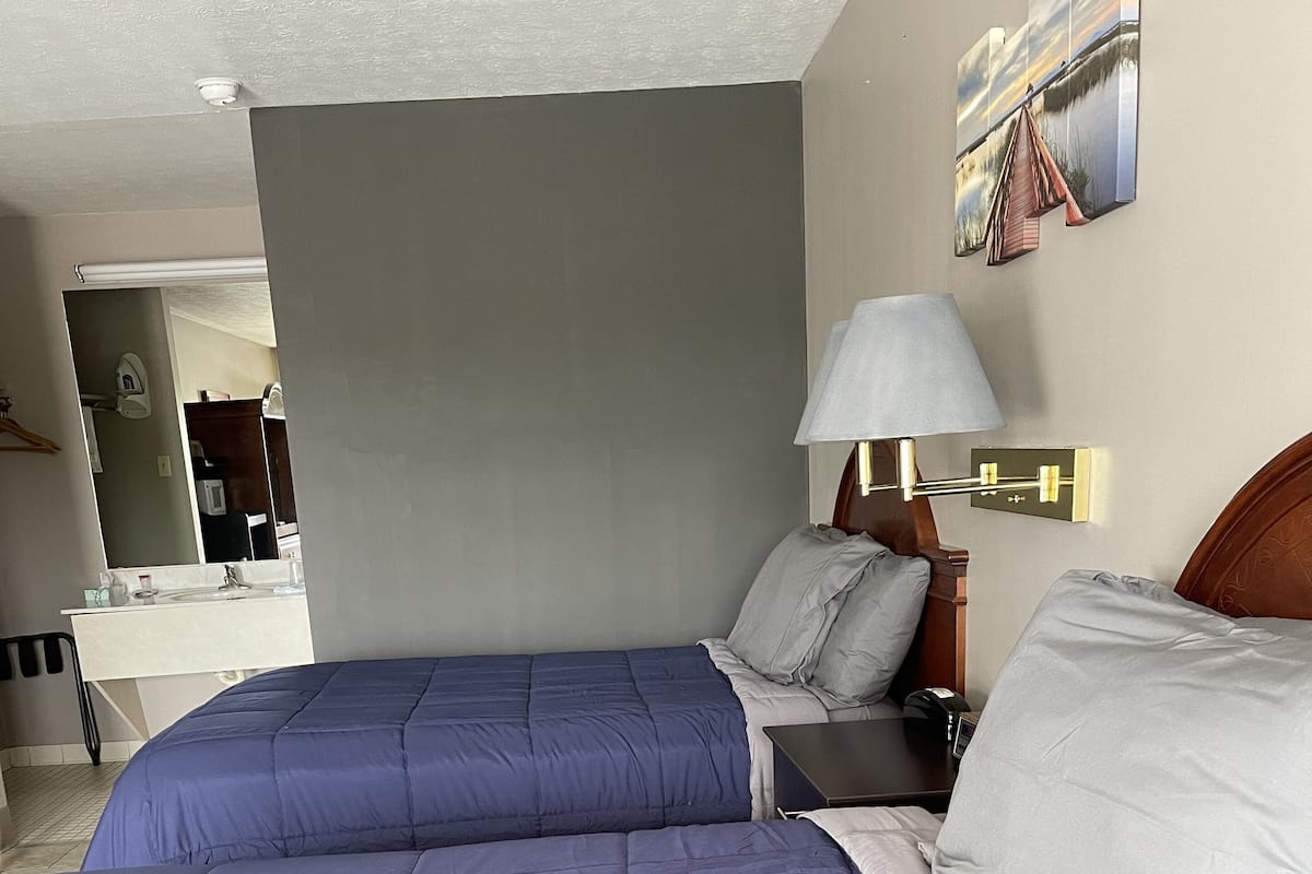 A hotel room with two beds, a large mirror, a bedside table with a lamp, and a wall-mounted artwork.