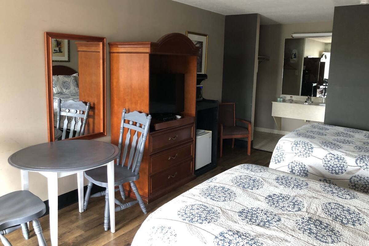 A hotel room with a bed, a desk with a television, a chair, a dresser, and a bathroom with a mirror.